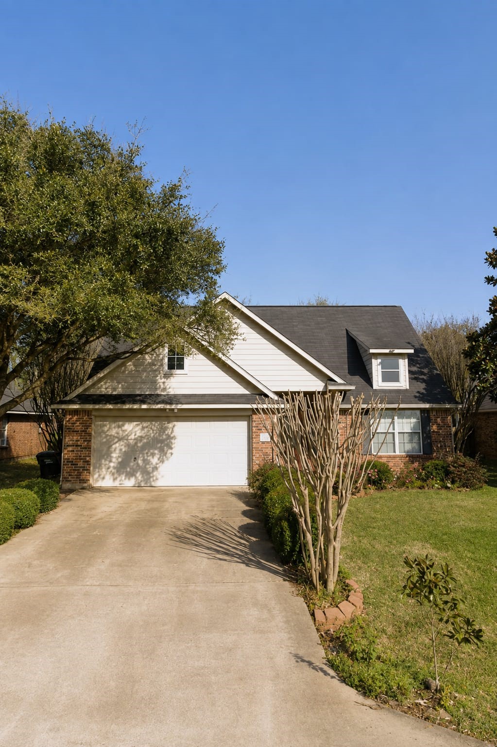 Charming brick home with a spacious two-car garage, nestled in a serene neighborhood. The well-maintained front yard features mature trees and a manicured lawn, perfect for outdoor enjoyment.