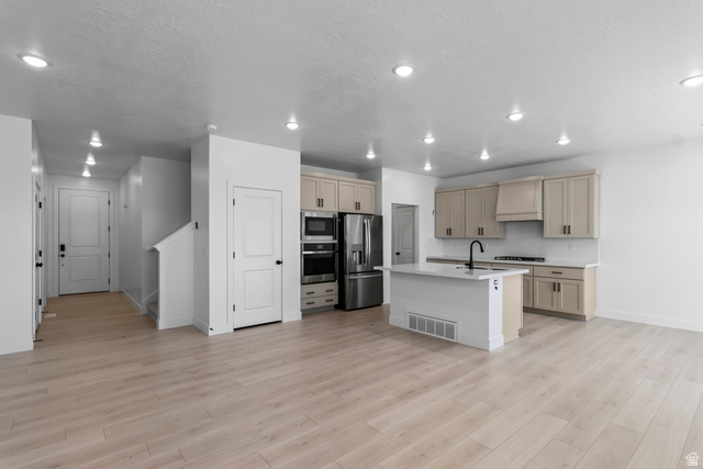 2770 West Aurora Avenue Mapleton, UT 84664 - Photo 2 of 16 Kitchen featuring stainless steel appliances, cream cabinetry, a kitchen island with sink, light stone countertops, and light wood finished floors