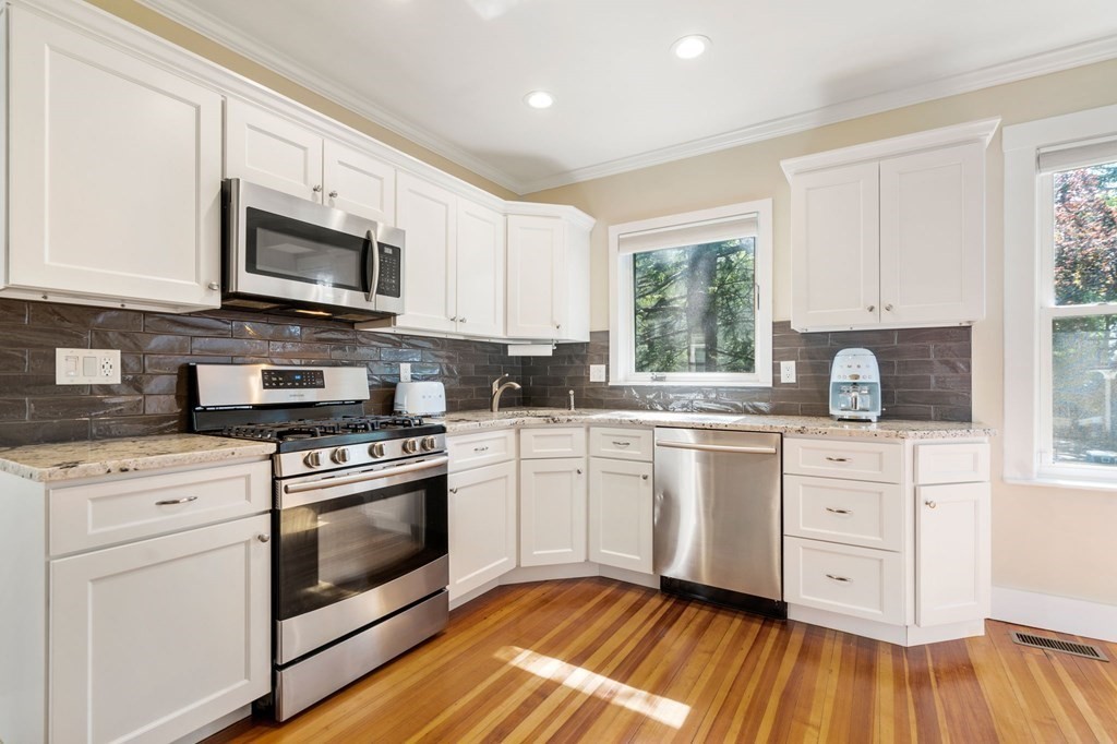 a white kitchen with granite countertop stainless steel appliances white cabinets granite counter tops and a window