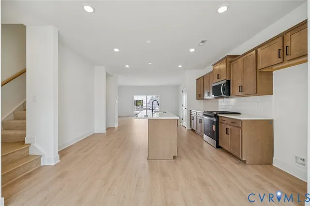 a kitchen with stainless steel appliances granite countertop a refrigerator a stove top oven a sink dishwasher and white cabinets with wooden floor