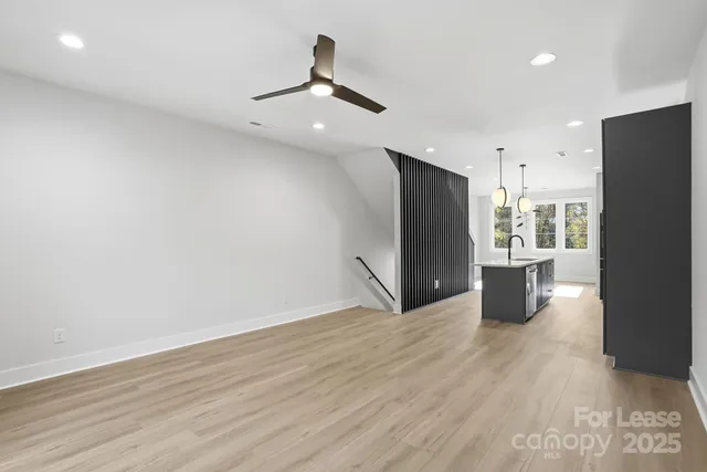 an empty room with wooden floor a ceiling fan and kitchen view