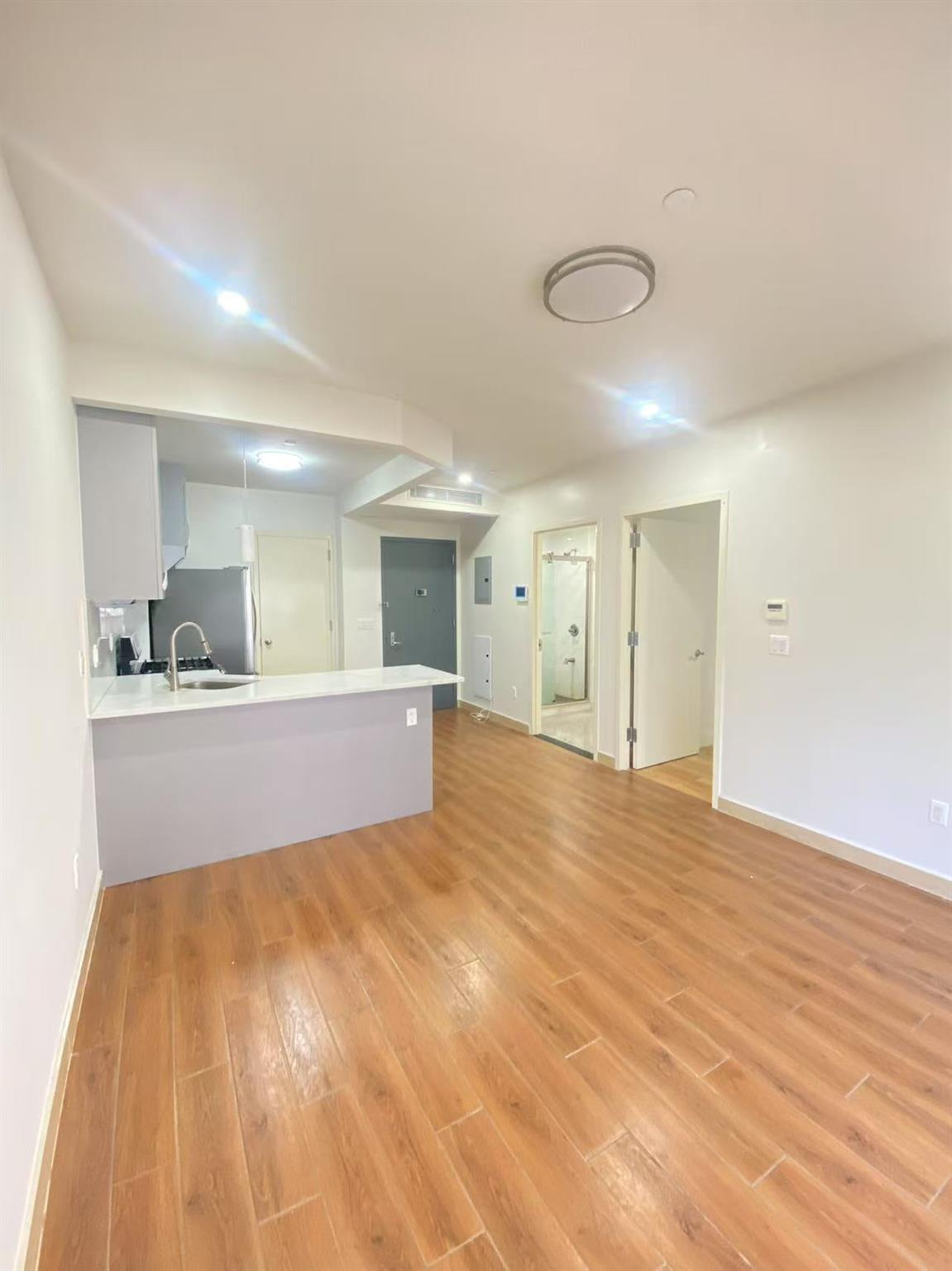 42-22 Crescent Street, Unit 3B Queens, NY 11101 - Photo 4 of 9 a view of kitchen and empty room with wooden floor