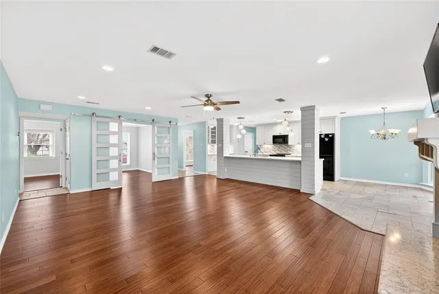 a view of an empty room with wooden floor and a kitchen
