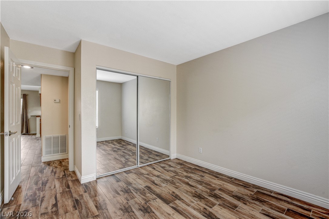 7200 West Pirates Cove Road, Unit 1026 Las Vegas, NV 89145 - Photo 21 of 35 This inviting bedroom features rich wood-look flooring and ample mirrored closet space, offering both style and function.