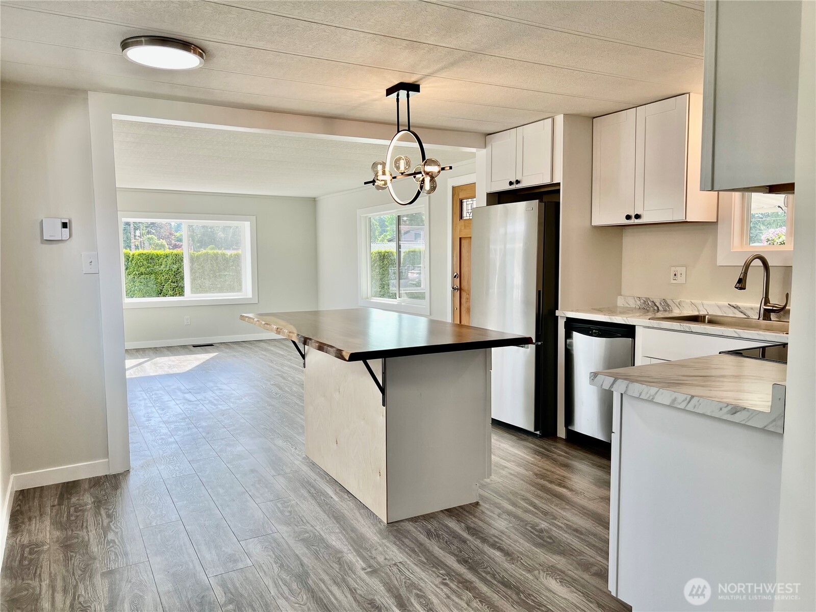 18501 52nd Avenue West, Unit 84 Lynnwood, WA 98037 - Photo 8 of 32 a kitchen with kitchen island granite countertop a stove a sink a refrigerator and white cabinets with wooden floor