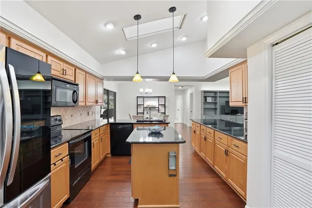 a large kitchen with stainless steel appliances kitchen island granite countertop a refrigerator a stove a sink dishwasher and wooden cabinets with wooden floor