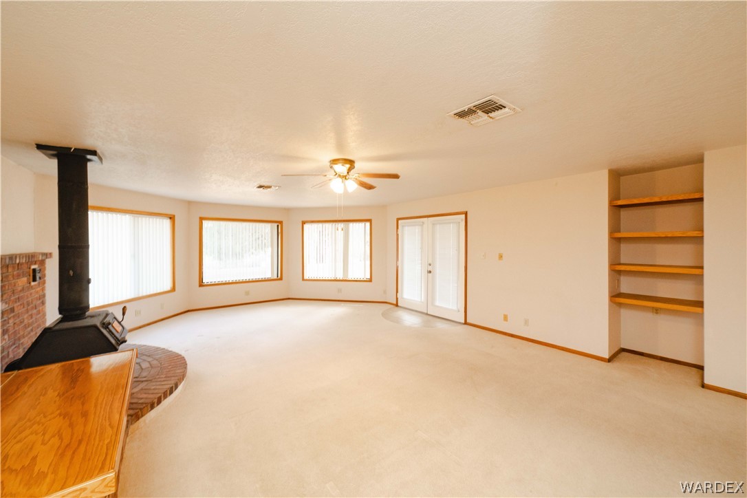2100 East Valley View Road Kingman, AZ 86409 - Photo 15 of 53 Spacious living area featuring a wood-burning stove with brick surround, multiple windows with vertical blinds, French doors, built-in shelving, and a ceiling fan