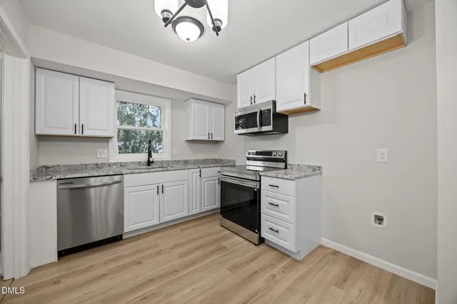 a kitchen with stainless steel appliances granite countertop a stove top oven a sink and white cabinets