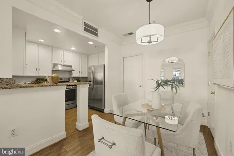 a kitchen with stainless steel appliances granite countertop a refrigerator a stove top oven a sink a dining table and chairs with wooden floor