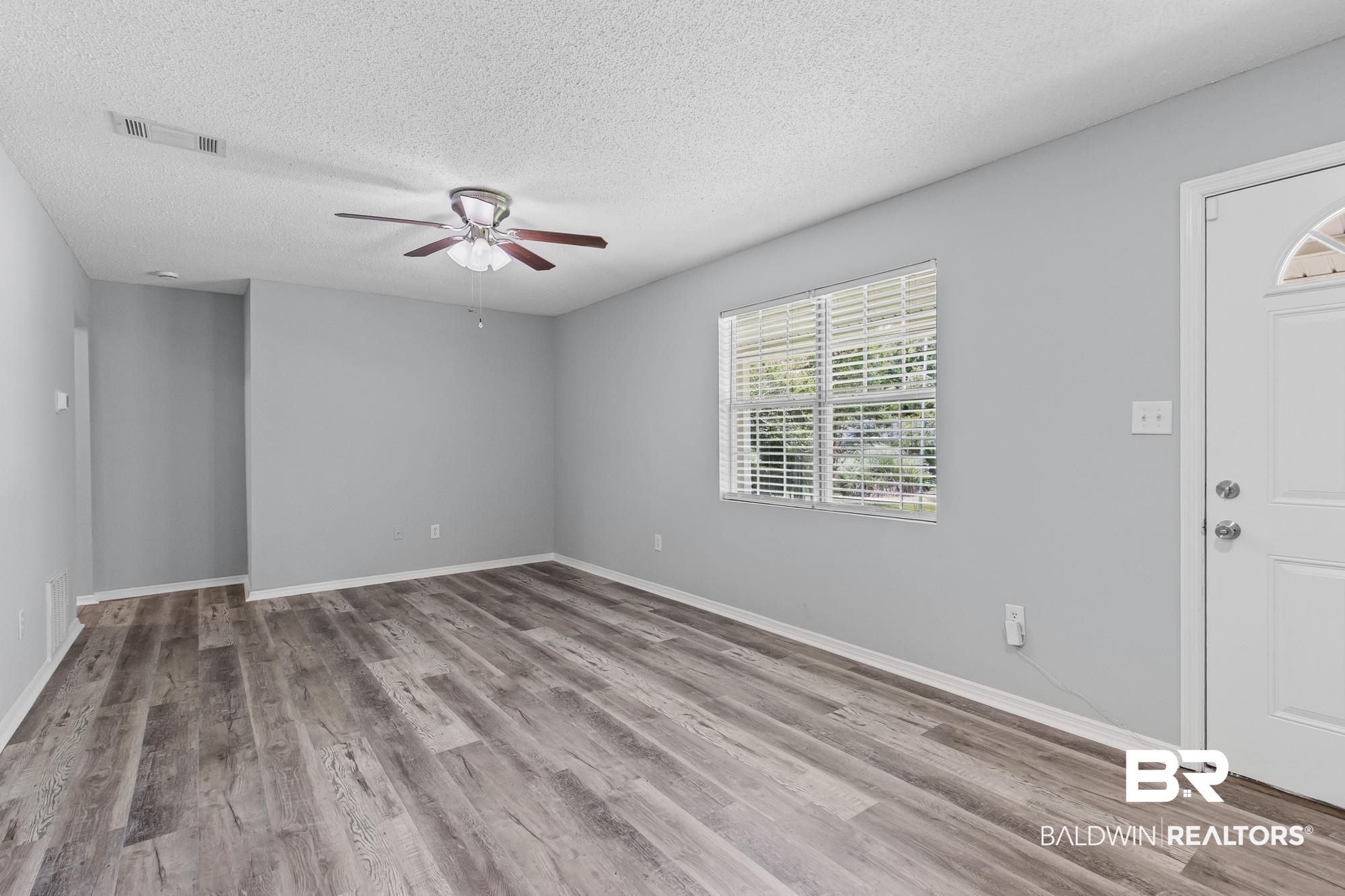 6933 Burbank Court Mobile, AL 36619 - Photo 8 of 25 Spacious room featuring wood-finish flooring, light gray walls, a window with horizontal blinds, a white paneled entry door with an arched glass insert, and a ceiling fan with light fixture