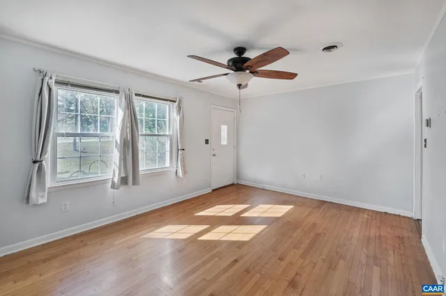 an empty room with wooden floor fan and windows