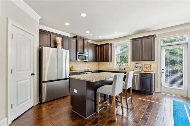 a kitchen with stainless steel appliances granite countertop a refrigerator a stove a sink a dining table and chairs with wooden floor