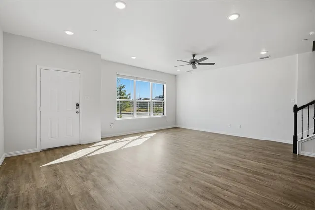 an empty room with wooden floor a ceiling fan and windows