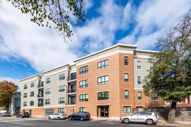 a front view of a building with lot of cars and trees