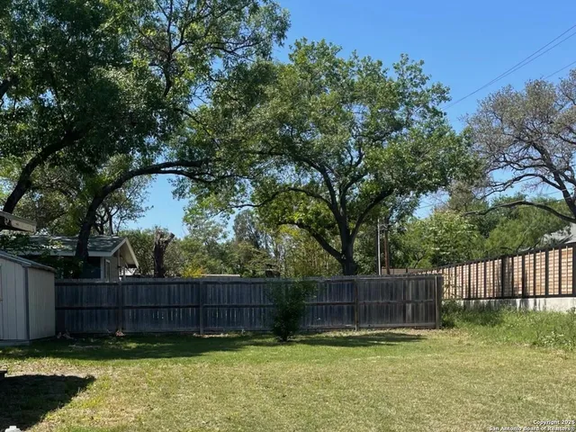 a view of a yard with large trees and wooden fence
