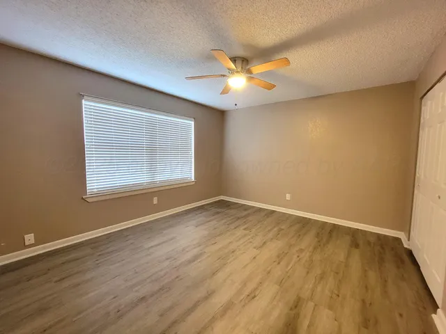 an empty room with wooden floor fan and windows