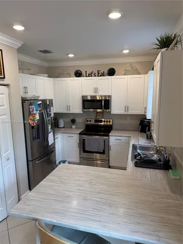 a kitchen with kitchen island a refrigerator stove and white cabinets with wooden floor