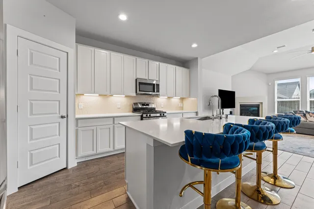 a kitchen with stainless steel appliances granite countertop a stove a sink a refrigerator a dining table and chairs with wooden floor