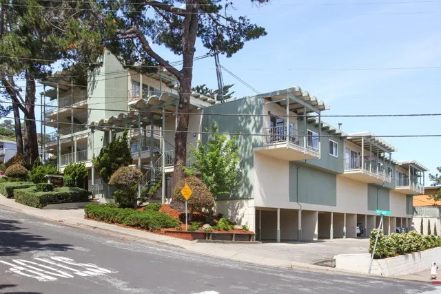 a front view of a building with a garden and trees