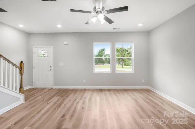 an empty room with wooden floor chandelier fan and windows