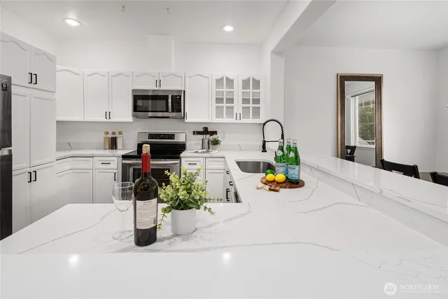 a kitchen with stainless steel appliances kitchen island granite countertop a sink white cabinets a stove top oven a dining table and chairs