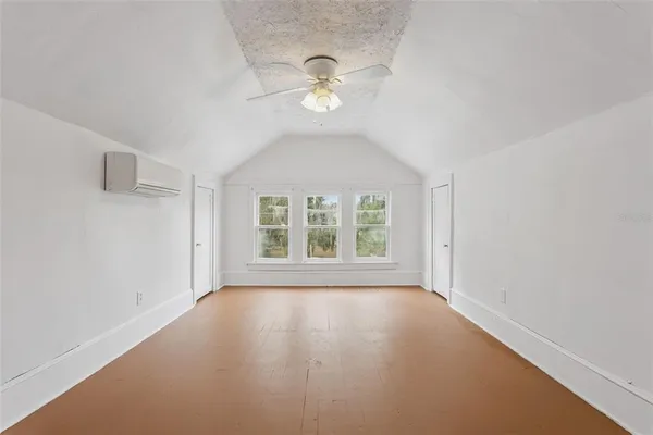 an empty room with wooden floor fan and windows