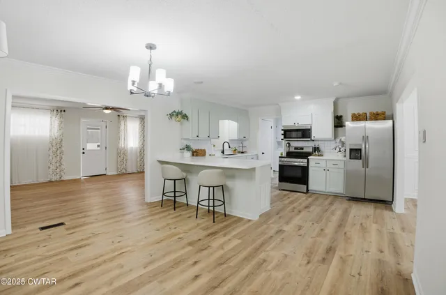 a kitchen with stainless steel appliances a dining table chairs stove refrigerator and cabinets