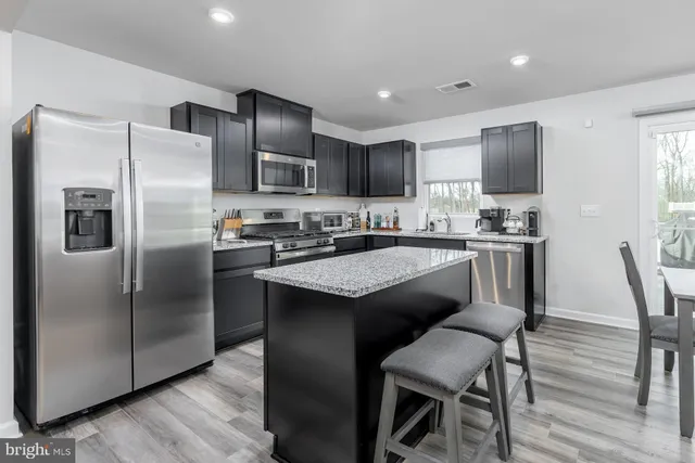 a kitchen with stainless steel appliances granite countertop a refrigerator a sink a stove a dining table and chairs