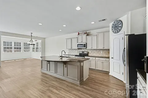 a kitchen with stainless steel appliances granite countertop a stove a sink a refrigerator and white cabinets with wooden floor