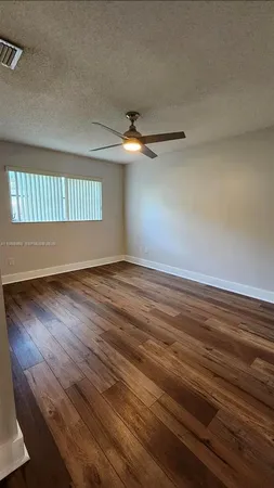 an empty room with wooden floor chandelier fan and windows