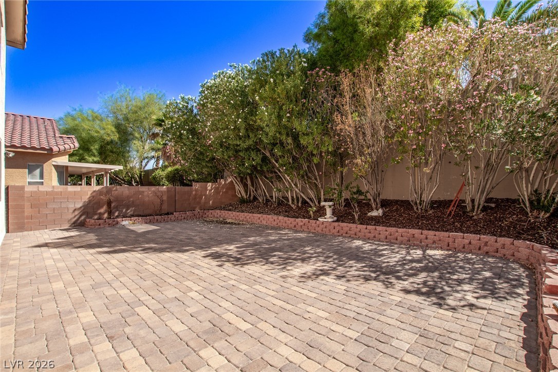 1477 Rancho Ridge Drive Henderson, NV 89012 - Photo 40 of 46 A neatly paved patio area is bordered by lush, mature landscaping under an azure sky.