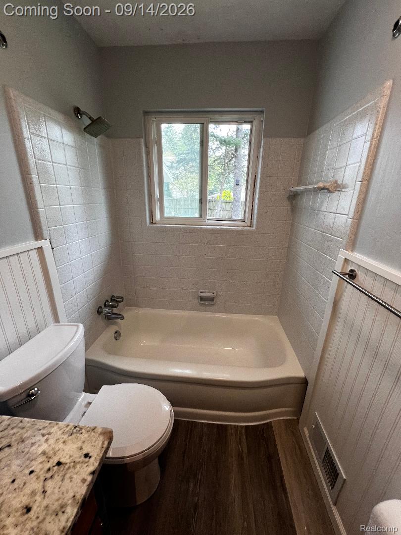 1615 Ladd Road Walled Lake, MI 48390 - Photo 17 of 28 Bathtub with white tile surround, window, and wood-finish flooring