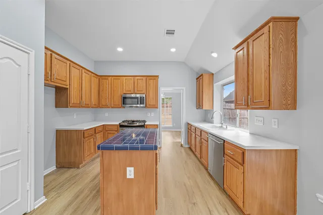 a kitchen with stainless steel appliances granite countertop wooden cabinets a sink dishwasher a stove and a refrigerator with wooden floor