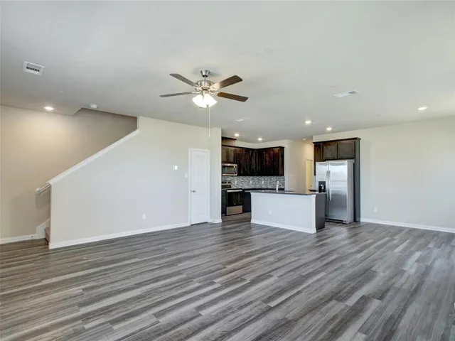 an empty room with wooden floor and a kitchen