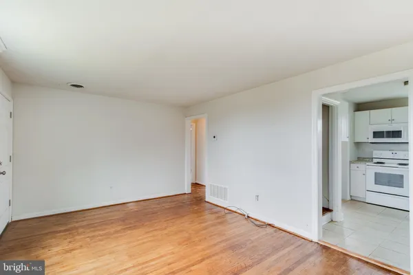 a view of empty room with wooden floor and kitchen