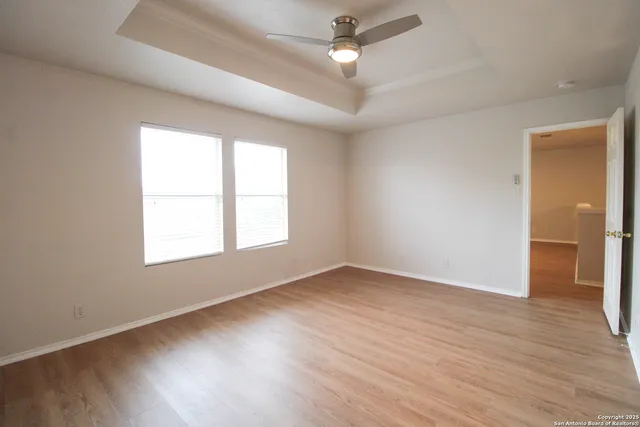 an empty room with wooden floor ceiling fan and windows