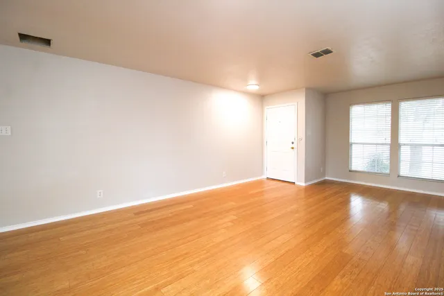 a view of an empty room with wooden floor and windows