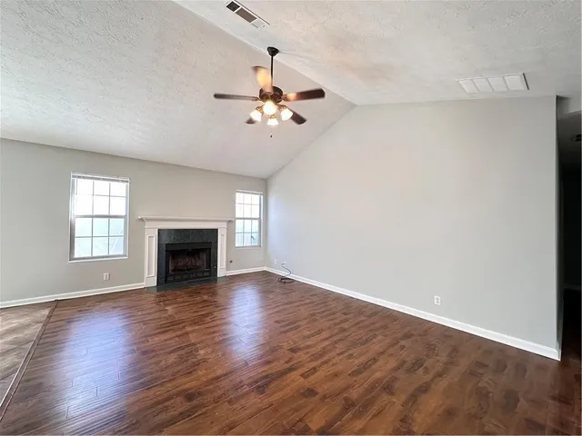 an empty room with wooden floor fan and windows