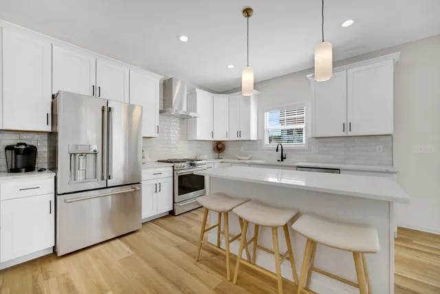 a kitchen with stainless steel appliances white cabinets a sink a stove a refrigerator and island with wooden floor