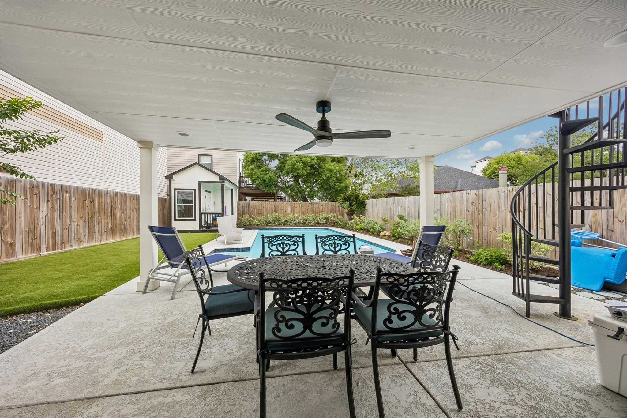 1420 Indiana Street Houston, TX 77006 - Photo 27 of 31 This outdoor space features a covered patio with a ceiling fan, and a view of a pool. It includes a spiral staircase and a small pool house, all surrounded by a privacy fence and landscaped greenery. Ideal for relaxation and entertaining.