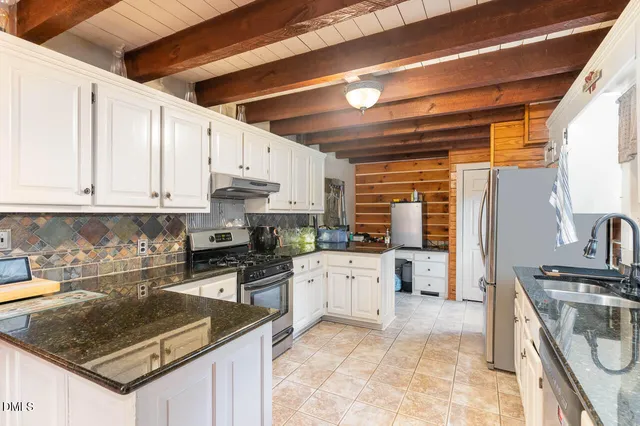 a kitchen with stainless steel appliances granite countertop a stove top oven a sink a dining table and chairs with white cabinets