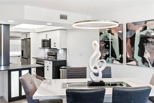 a kitchen with stainless steel appliances kitchen island granite countertop a refrigerator a stove a sink and white cabinets with wooden floor