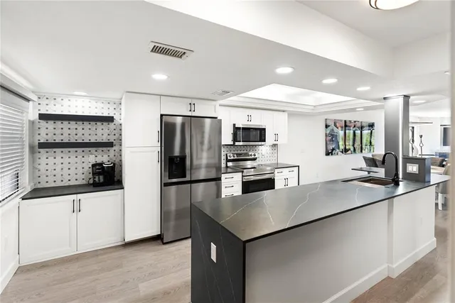 a kitchen with stainless steel appliances a sink a stove a refrigerator with white cabinets and wooden floor