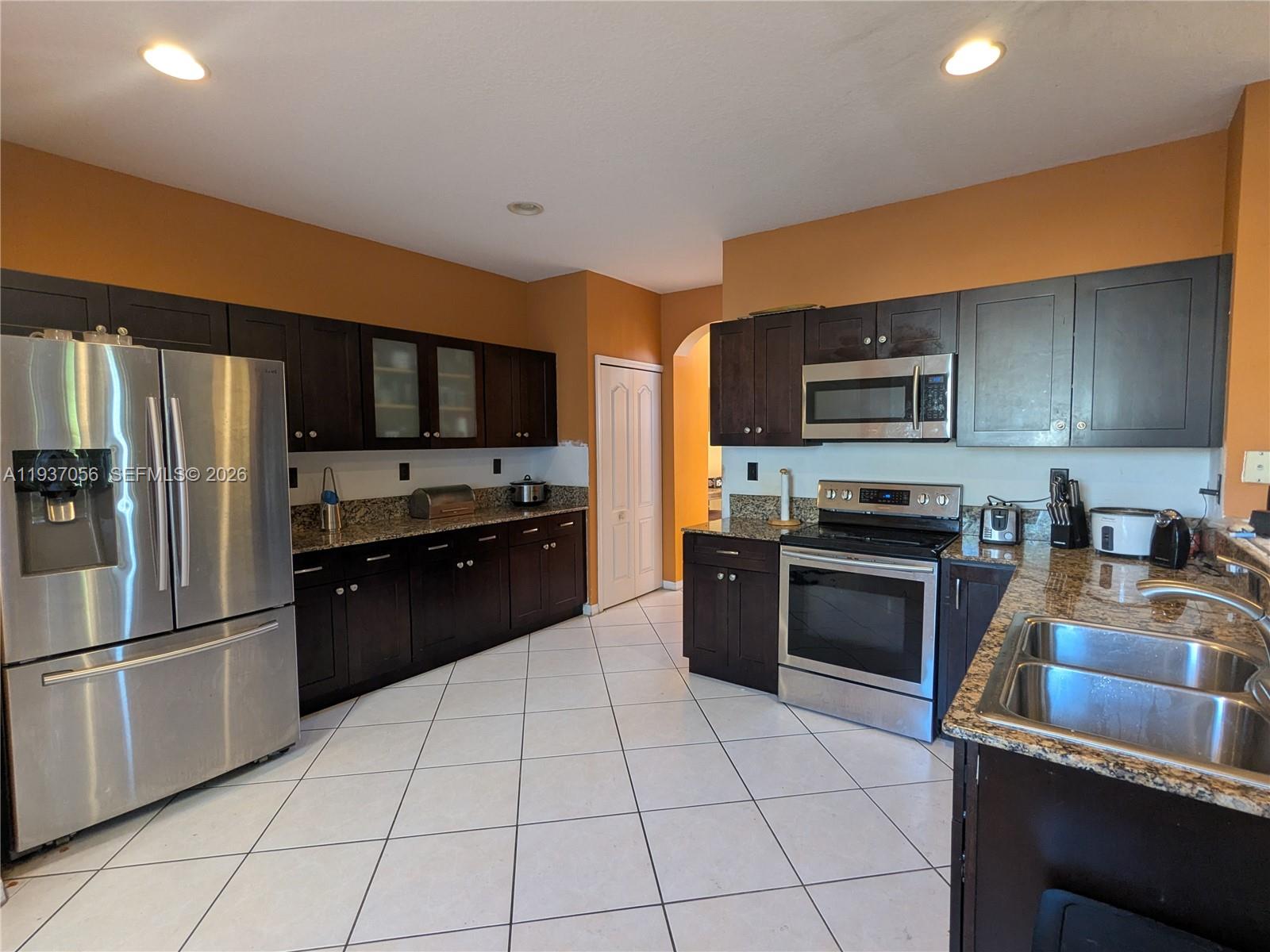 12641 Southwest 28th Street Miramar, FL 33027 - Photo 2 of 52 Modern kitchen featuring stainless steel appliances, dark wood cabinetry, and granite countertops