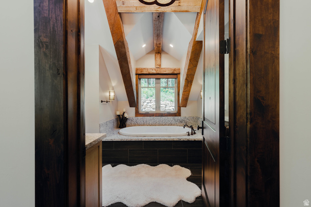 1667 West Tollgate Cyn Road Coalville, UT 84017 - Photo 11 of 61 Attic bathroom featuring exposed wood beams, a built-in soaking tub with a dark tile surround, a wood-framed window, recessed lighting, and sconce lighting