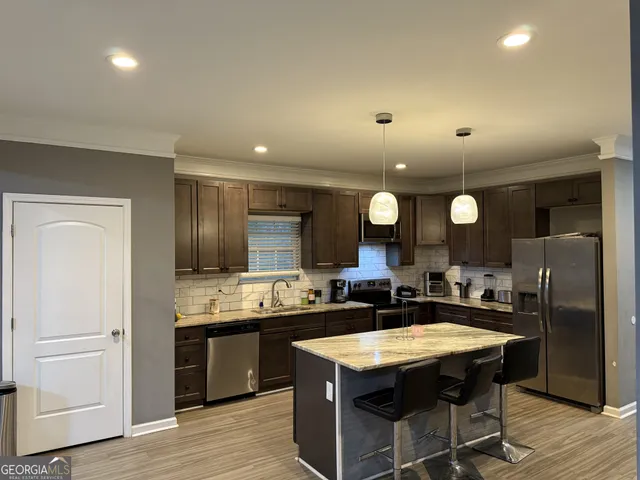 a kitchen with stainless steel appliances granite countertop a sink a stove a refrigerator and island with wooden floor