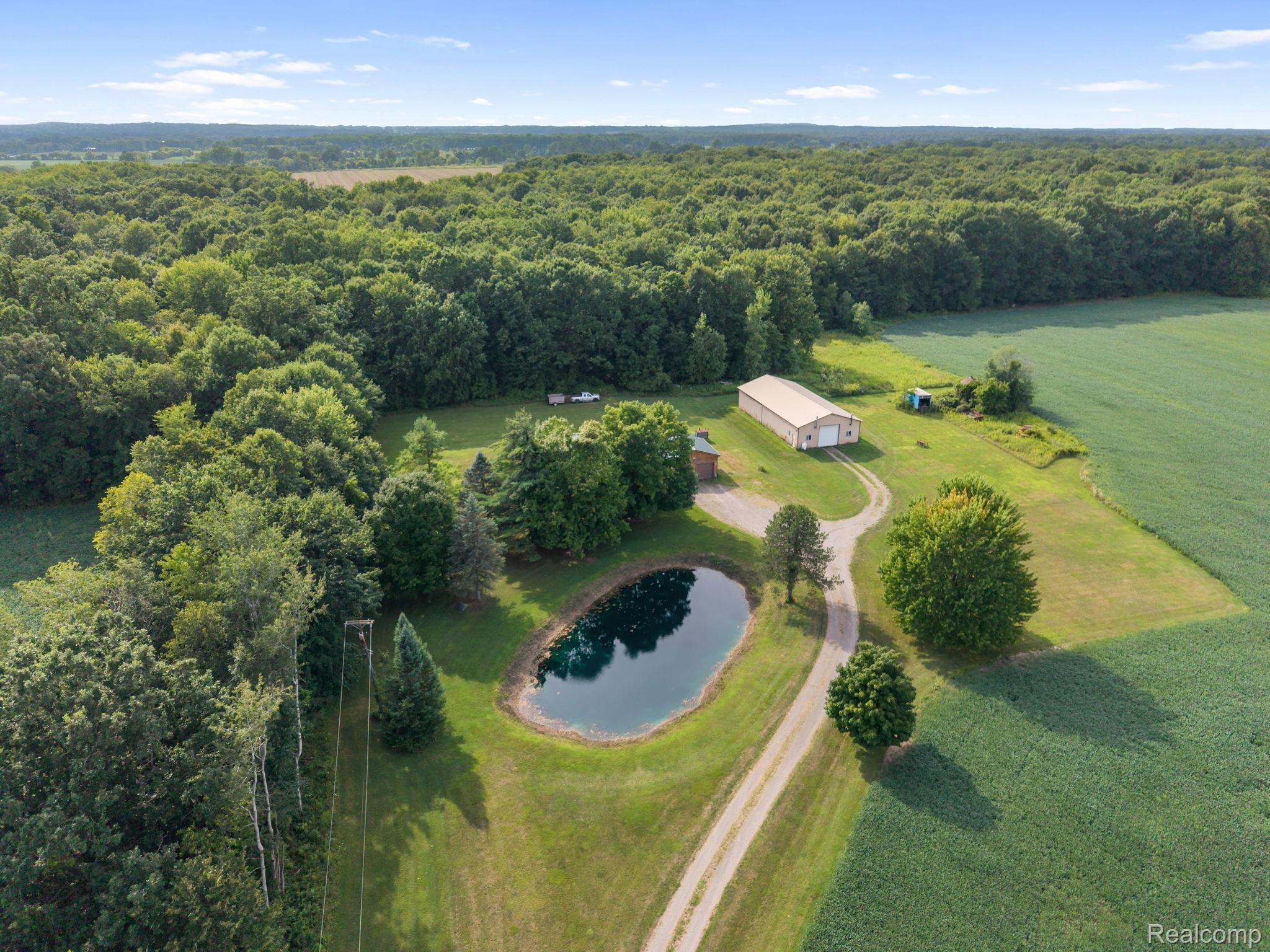 76565 McFadden Road Armada, MI 48005 - Photo 88 of 95 Expansive property featuring a private pond, large detached outbuilding, mature trees, open green spaces, and a dirt driveway