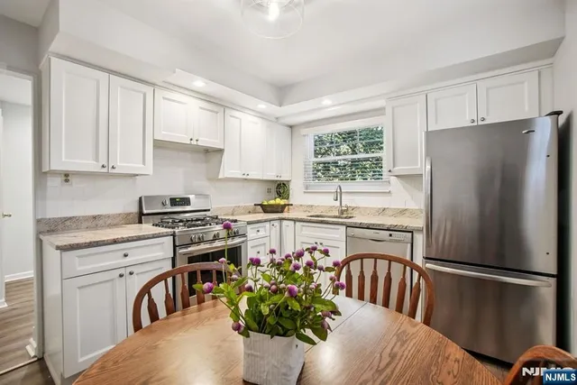 a kitchen with stainless steel appliances granite countertop a refrigerator a stove a sink dishwasher and white cabinets with wooden floor