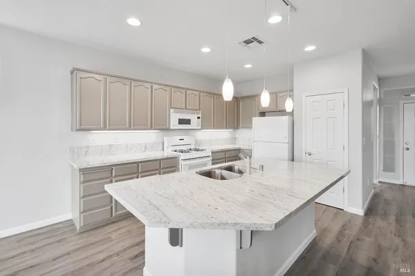 a kitchen with stainless steel appliances granite countertop a kitchen island a stove a sink a refrigerator and white cabinets with wooden floor