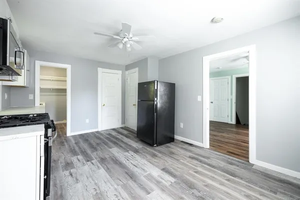a view of an empty room with wooden floor and a kitchen